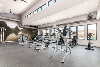 A gym with a variety of exercise equipment and a mountain mural on the wall.